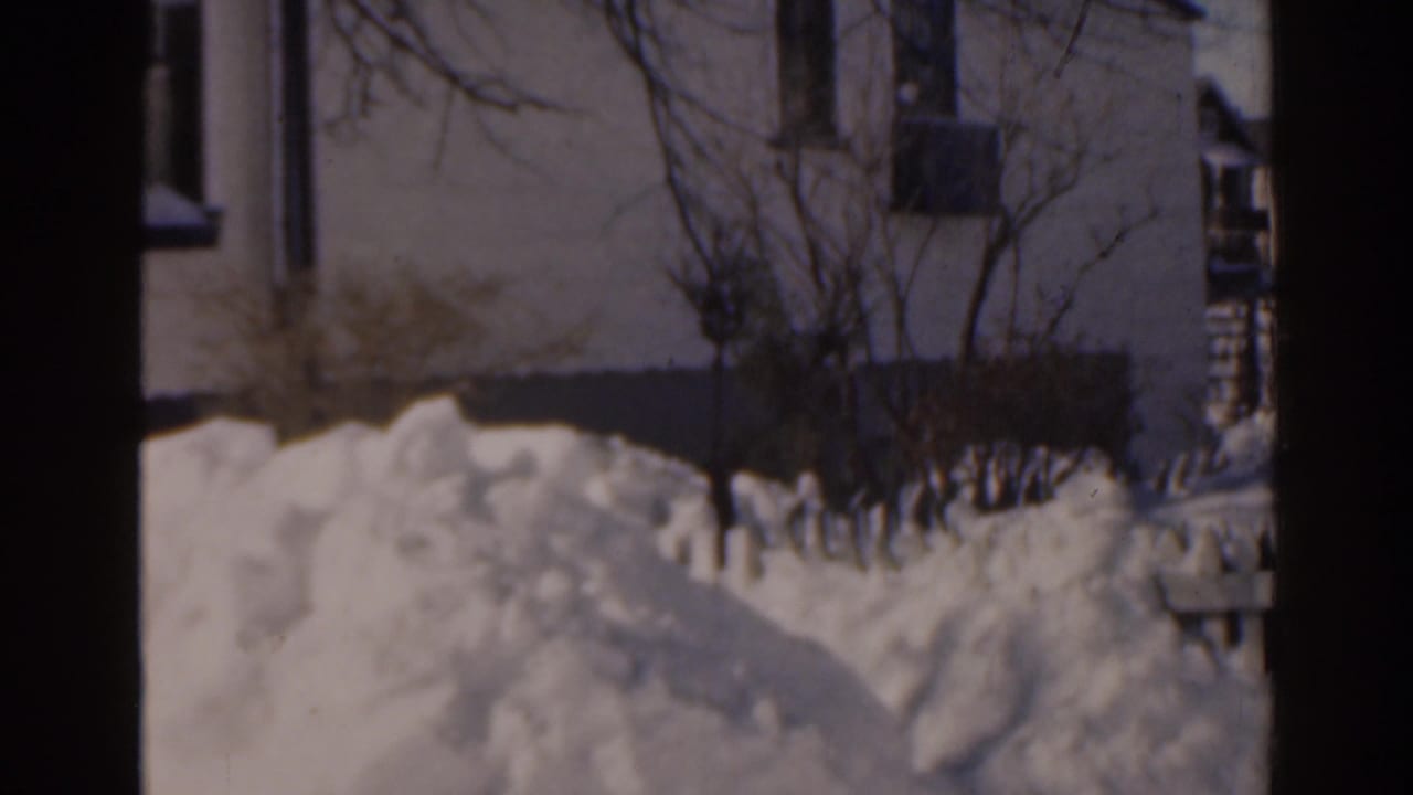 Snowbanks in front of a house with bare shrubs and dark film borders.