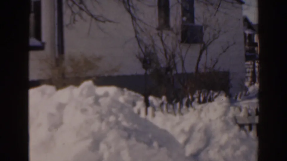 1963 Florida 8mm frame showing deep snow piled near a residential building, with bare shrubs and visible film-frame edges.