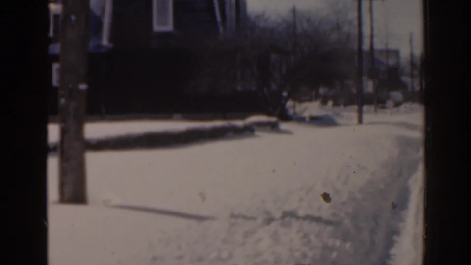 1963 Florida 8mm frame of a snowy residential street edge with a utility pole, winter trees, and houses beyond the snow.