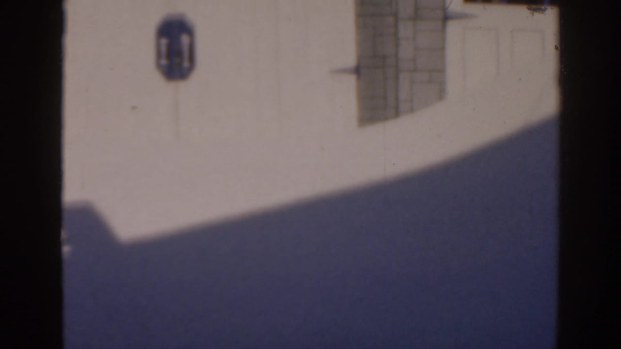 White exterior wall with blue wall sign, gridded window, and broad shadow.