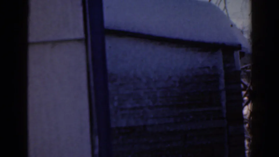 Blue-shifted 1963 8mm view of a rural wall or outbuilding edge beside snow-covered ground in the Florida-labeled clip.