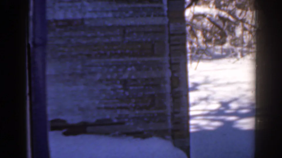 1963 Florida-labeled home-movie frame with a brick or stone wall, a snowy opening, and bare tree shadows across the ground.