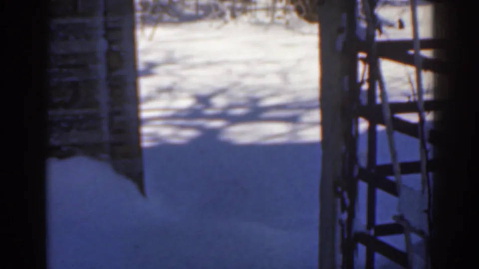 1963 Florida 8mm frame showing snow on the ground viewed from a shadowed doorway or window, with brickwork and a ladder nearby.