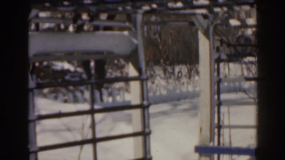 1963 Florida home-movie frame shows snow on a metal structure with railings and leafless branches behind it.