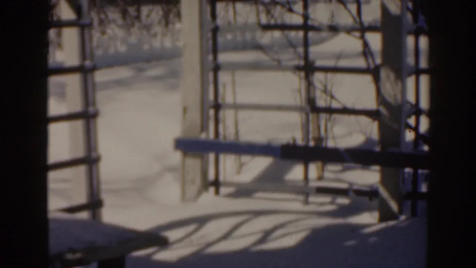 1963 8mm frame shows a snowy metal framework, railings, and dark shadows crossing the winter ground.