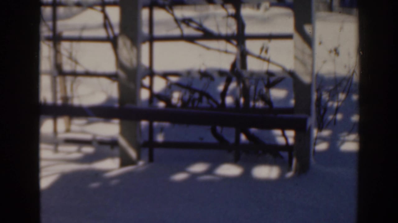 Snow-covered yard seen past dark porch or fence framing, with winter shadows across the ground.