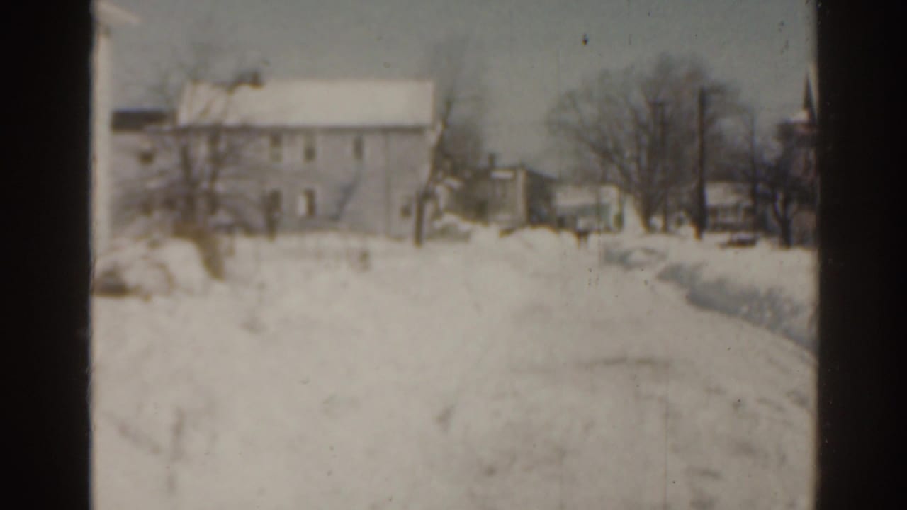 Snow-covered house and yard with bare trees and a plowed or worn path through the snow.