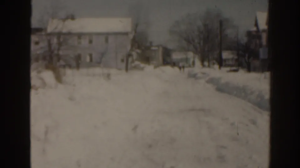 1963 Florida frame showing a snow-covered house and yard beside a dark film-frame edge, with bare trees and a snowy path visible.