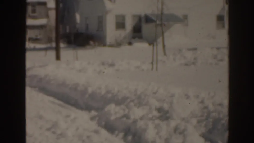 1963 Florida 8mm frame showing a snow-covered roadside lawn and residential house under muted winter light.