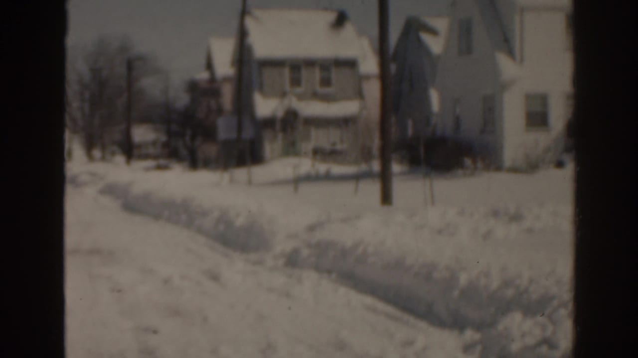 Snow-covered suburban houses and a utility pole along a quiet residential street.