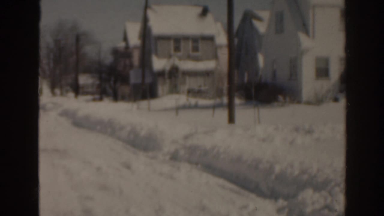 Snowy residential view with houses, bare trees, and a utility pole.