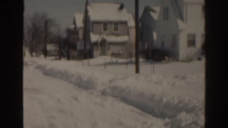 1963 Florida home-movie view of a snow-covered neighborhood with pale houses, a utility pole, and winter-bare trees.