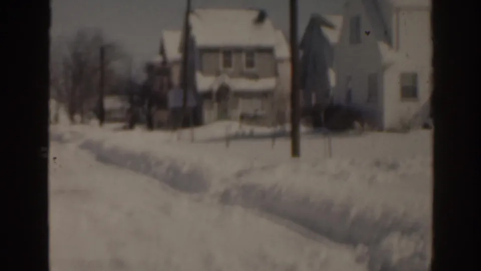 1963 Florida 8mm frame with snow piled beside a residential path, houses in the background, and bare trees nearby.