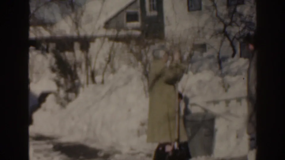 1963 Florida home-movie frame showing two women in long coats near deep snow outside a residential house.