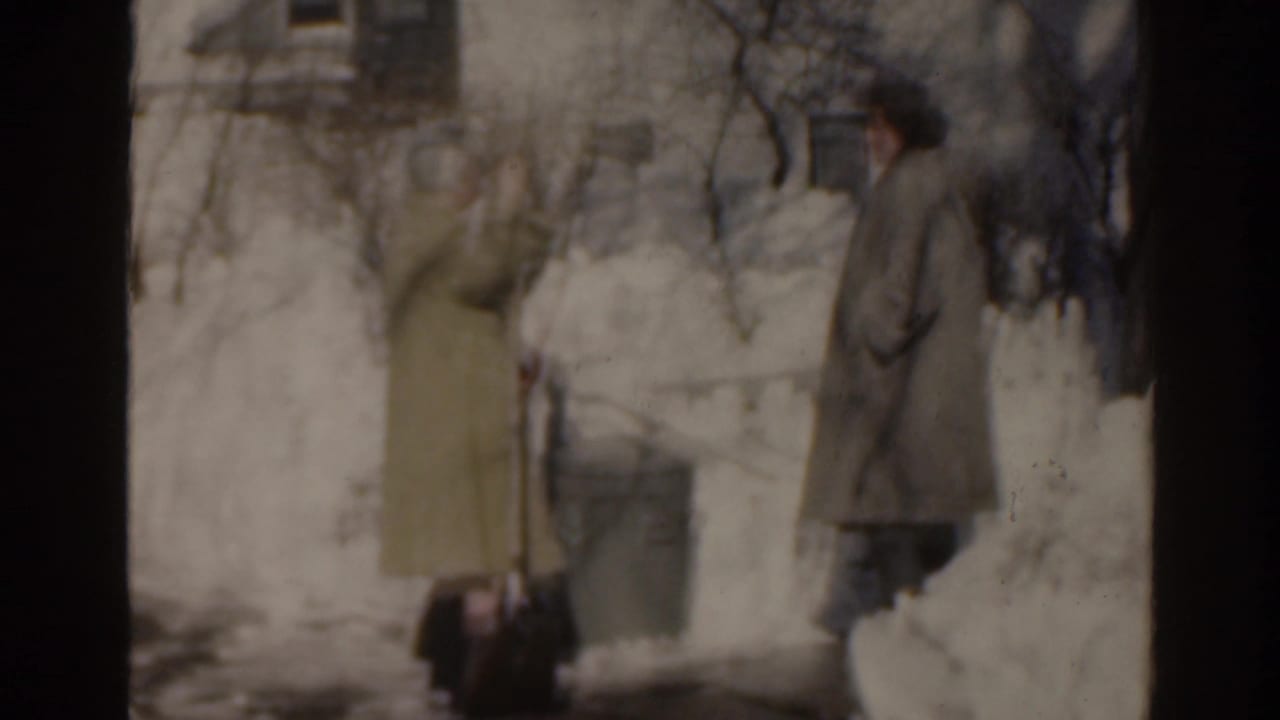 A woman with a shovel faces another woman beside deep snow.