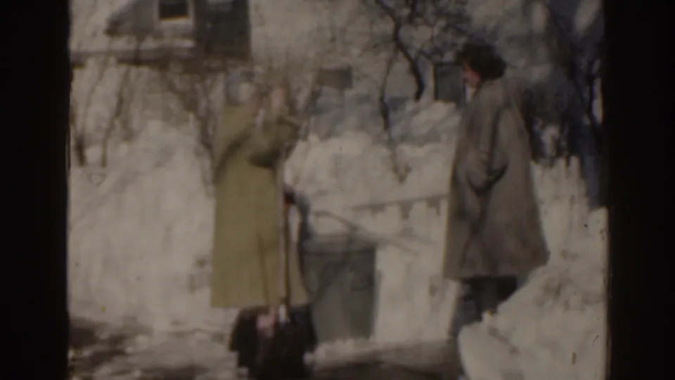 Soft 8mm frame of two women in coats standing beside high snowbanks outside a Florida residence in 1963.