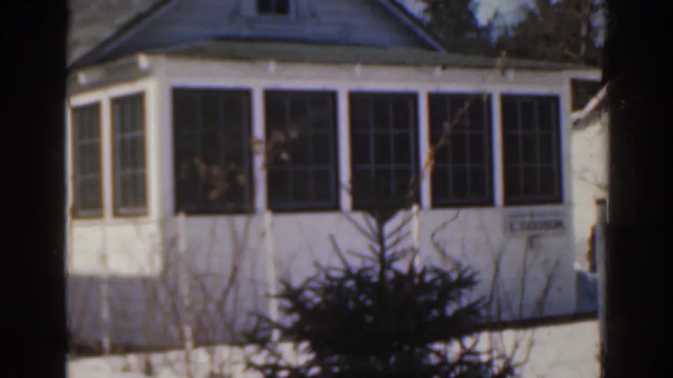 1963 Florida 8mm frame showing the bungalow facade, bay-like window section, foreground shrubs and a small readable E. DOOSON nameplate.