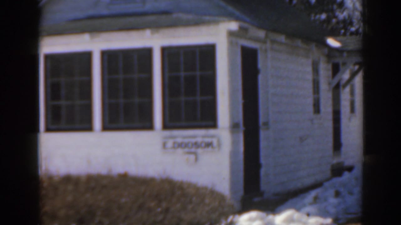 White house exterior with bay windows, snow on the ground, and a dark doorway.