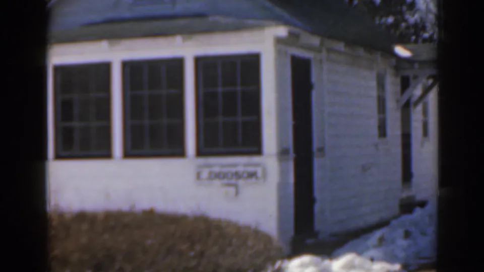 1963 Florida home-movie frame showing a white clapboard house, bay window, snowbanks, and an E. Dodson nameplate.