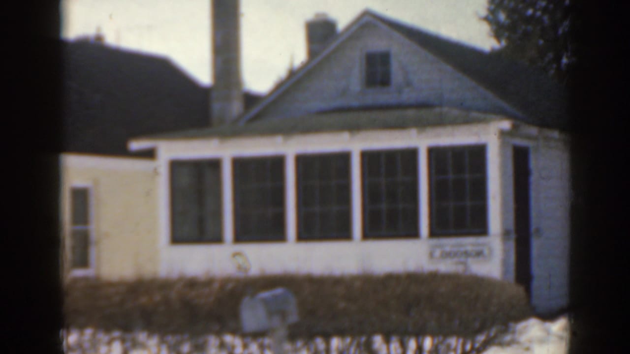 Small white house with enclosed front windows, shrubs, and snow patches in the yard.