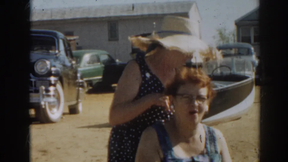 1963 New Jersey home-movie frame showing two women by a small boat as the hat-wearing woman turns away from the camera.