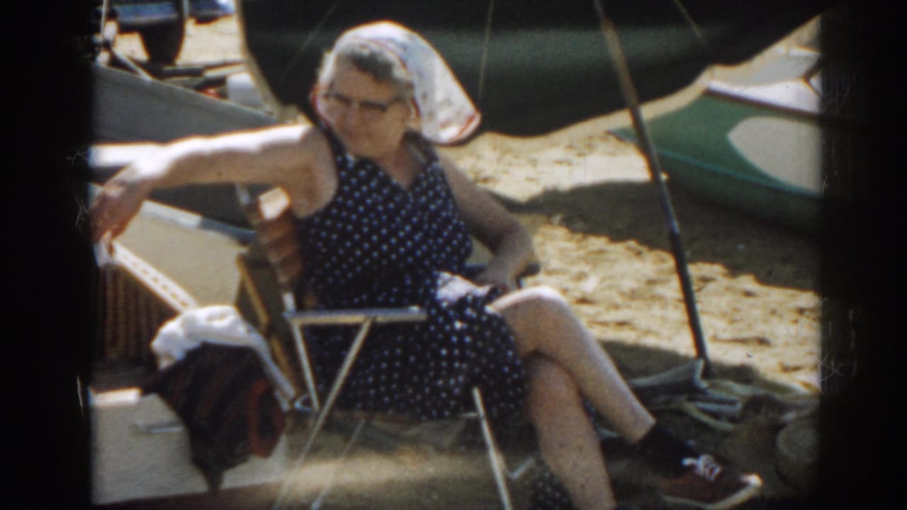 Woman in a polka-dot romper sits in a folding chair on a sandy beach.