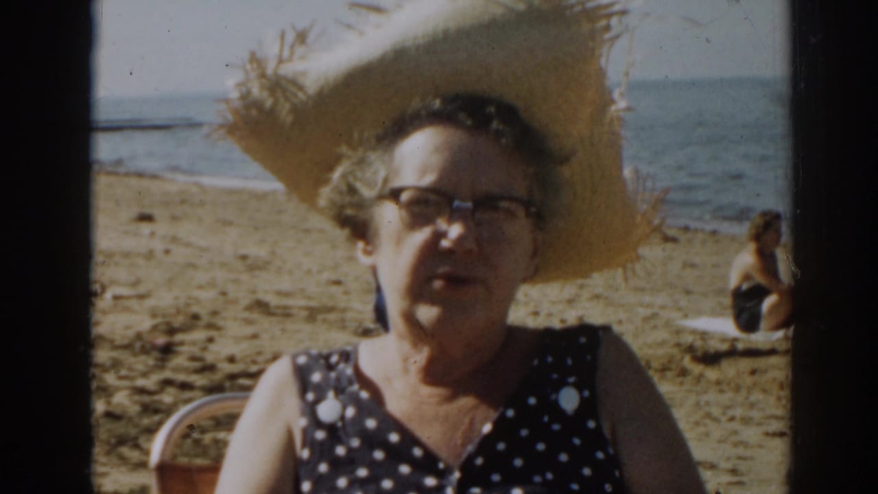 Woman in beachwear looks toward the camera with ocean and sand behind her.