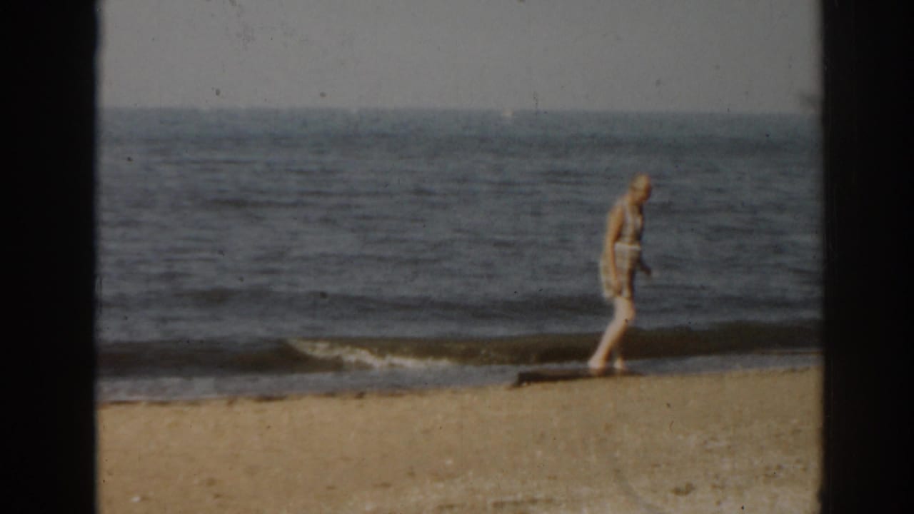 Woman continues walking along the beach beside a low breaking wave.