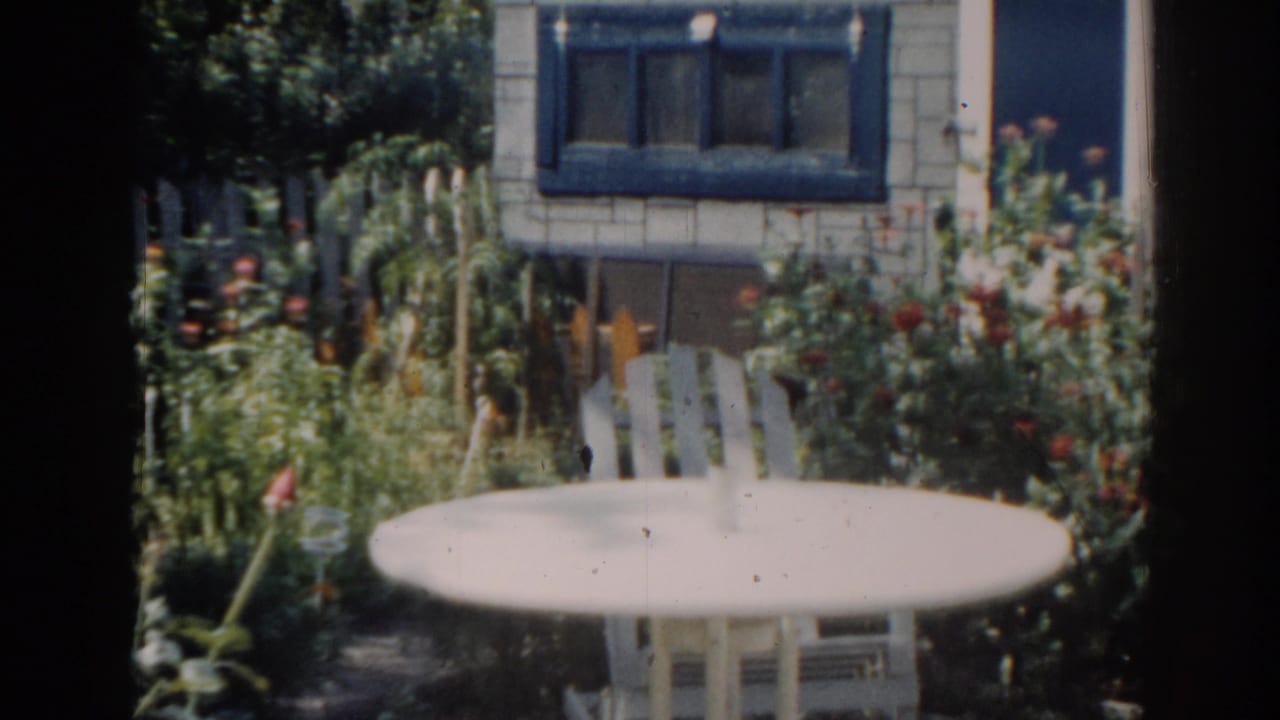 1963 New Jersey 8mm frame showing a quiet backyard garden with white patio furniture and a blue-trimmed house window.