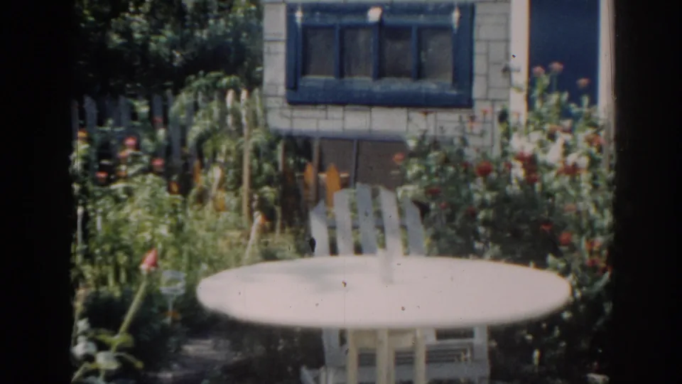 1963 New Jersey 8mm frame showing a quiet backyard garden with white patio furniture and a blue-trimmed house window.