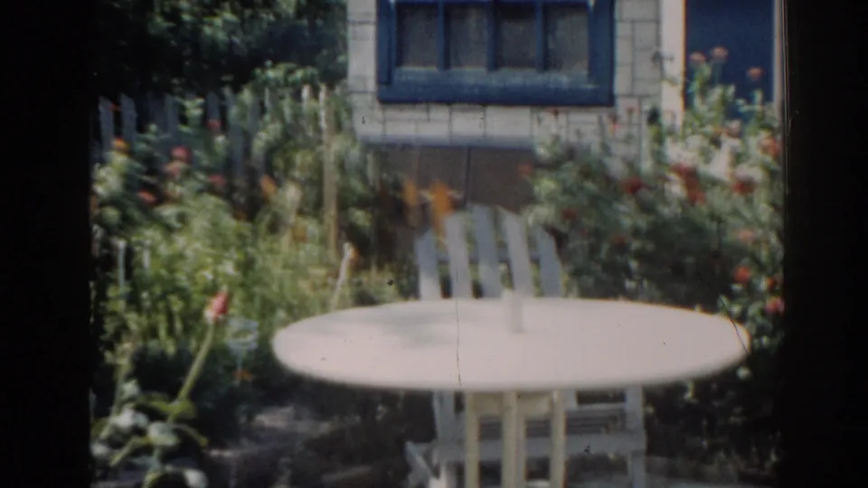 1963 New Jersey 8mm frame of the backyard table and chair, softened by handheld focus and aged film texture.