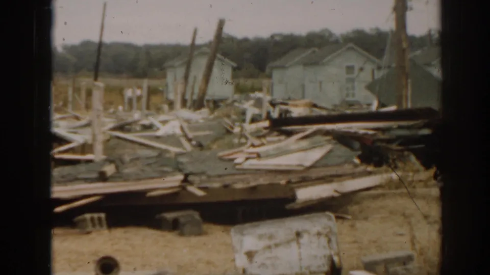 1963 New Jersey 8mm aftermath frame with scattered tornado debris, a white barrel, houses, poles, and dry grass.