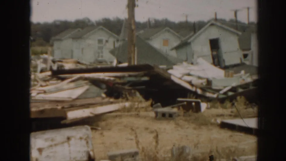 1963 New Jersey tornado aftermath showing damaged houses, scattered boards, an open doorway, poles, and debris in 8mm footage.