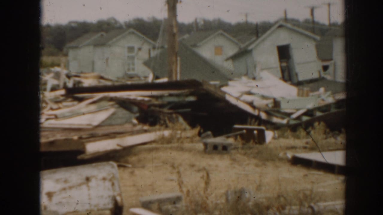 Small pale structures behind scattered boards and debris in a dry outdoor lot.