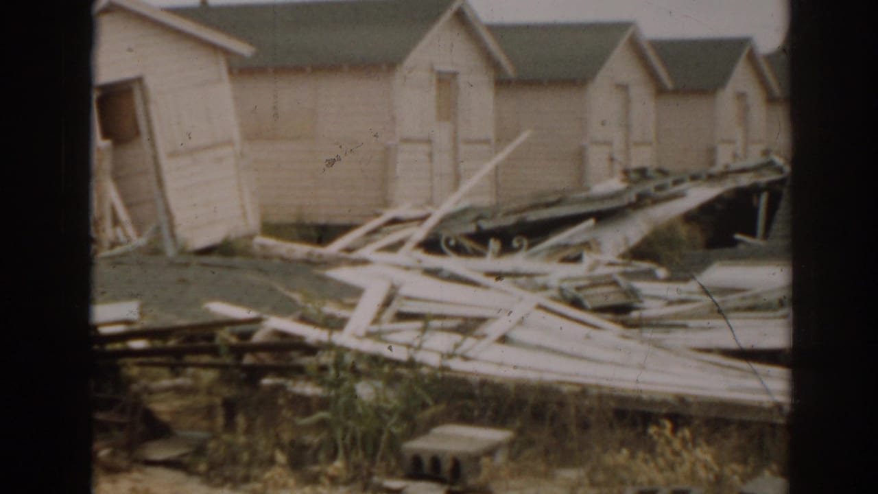 Row of wooden shacks with broken planks and roofing debris across the yard.