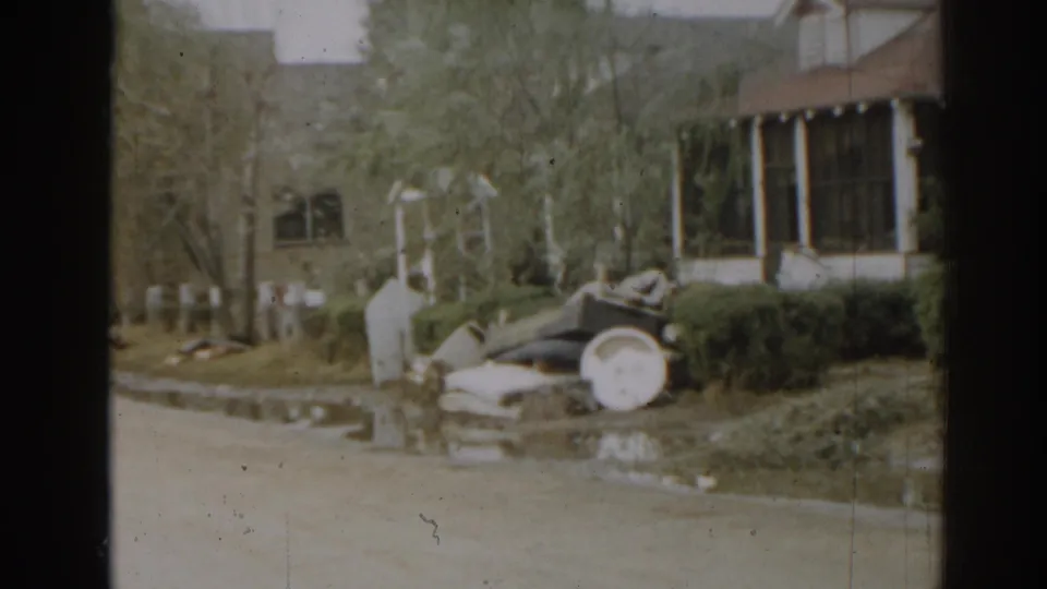 1963 New Jersey home-movie view of a suburban yard, porch, shrubs, and household items near the street.