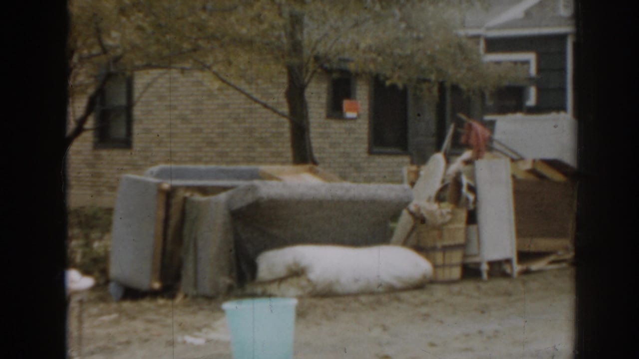Discarded furniture and bedding outside a brick house with a tree and metal bin nearby.
