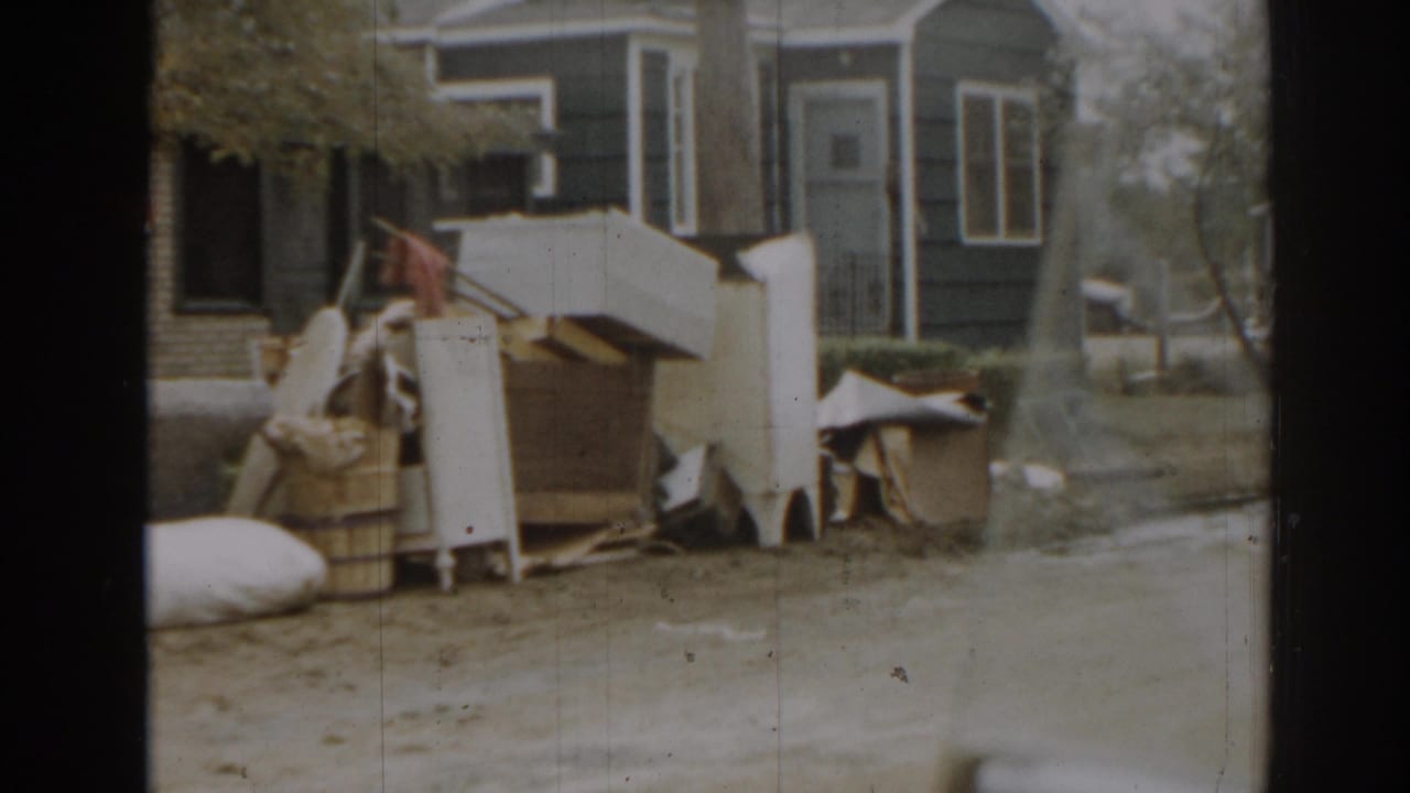 1963 New Jersey home-movie frame showing household debris and furniture piled outside near a blue house and porch.