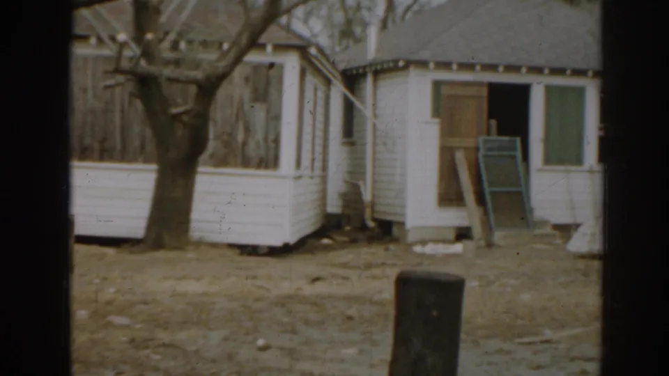 1963 New Jersey frame showing a white shed or outbuilding with boarded windows beside a bare residential yard.