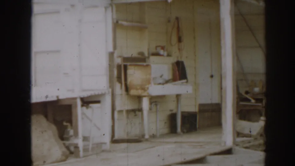 1963 New Jersey farm outbuilding porch showing a worn utility sink, shelves, tools, and pale exterior siding.