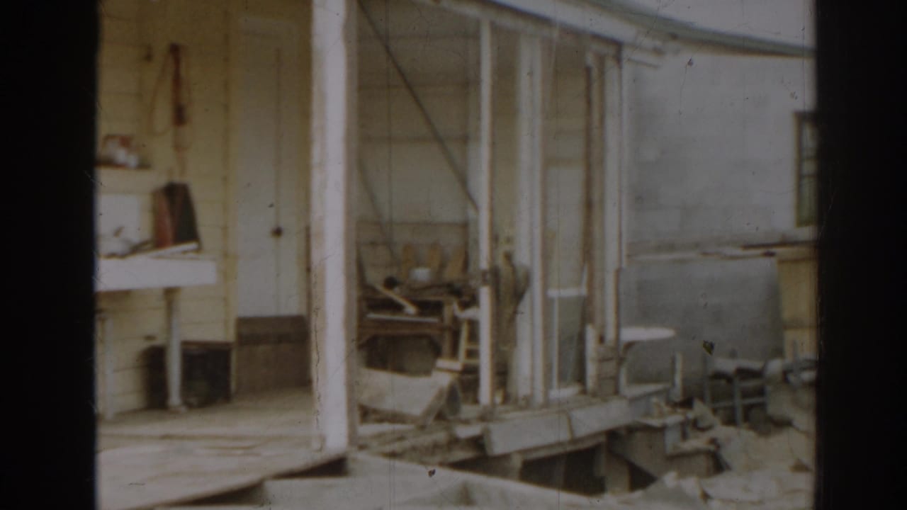Damaged house exterior with porch, debris, and household objects in the yard.