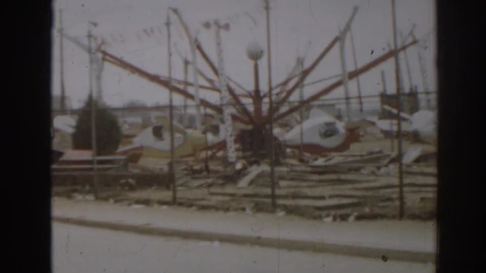 1963 New Jersey frame showing a damaged amusement-ride-like structure with metal arms, fence rails, and scattered debris.