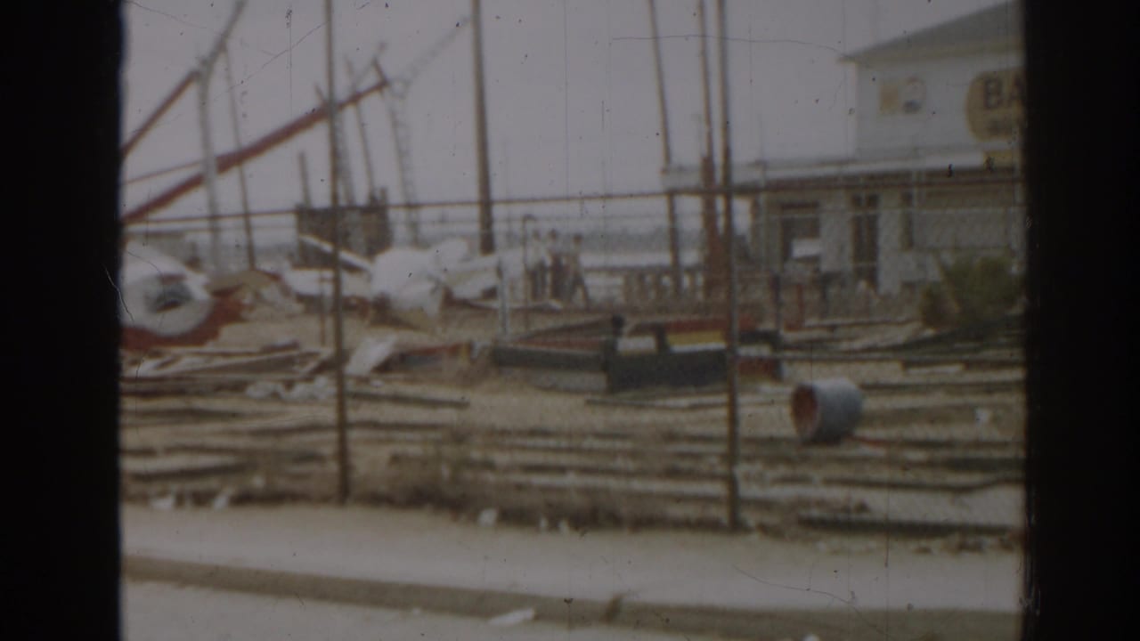 Collapsed ride frames and debris stand near a building with a bath house sign in the background.