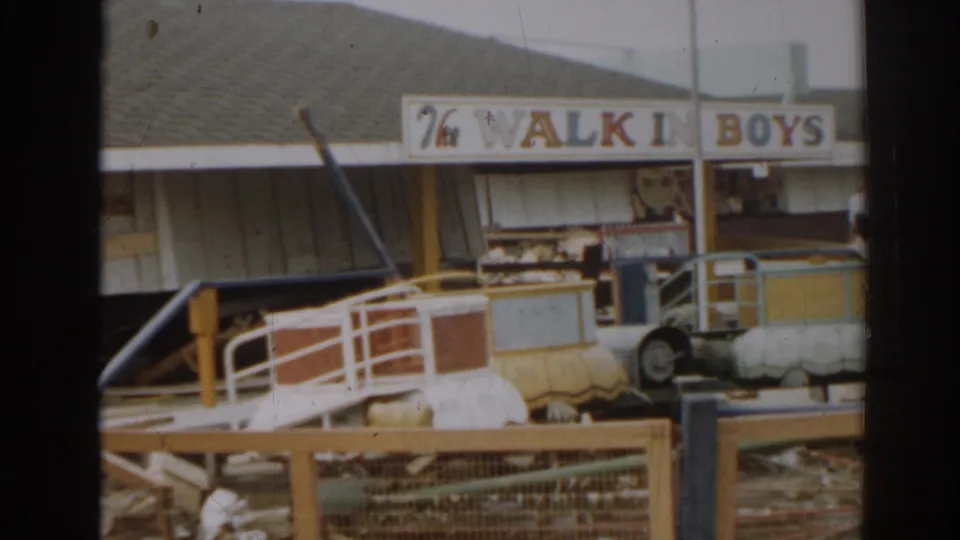 A faded 8mm frame from 1963 New Jersey showing a walk-in sign, railings, debris, and a small amusement ride vehicle.