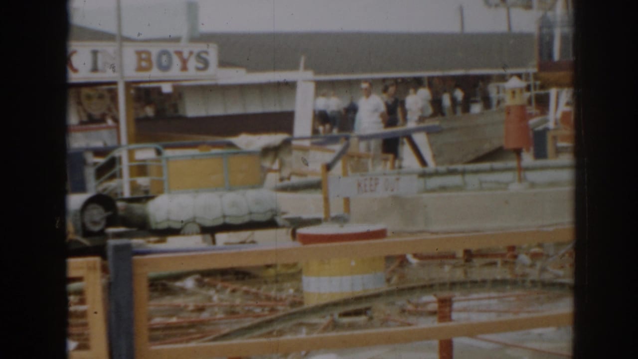 Amusement park damage with a BOYS sign, railings, debris, and several people near the ride area.