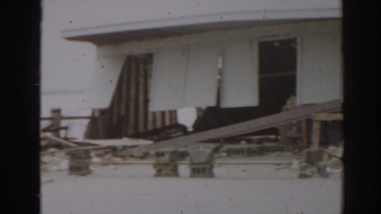Damaged white building with debris beneath raised wall panels.