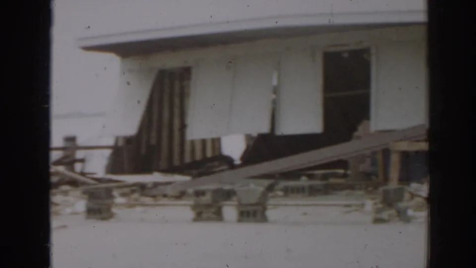 1963 New Jersey 8mm frame showing a damaged white building with broken material and debris near the foundation.