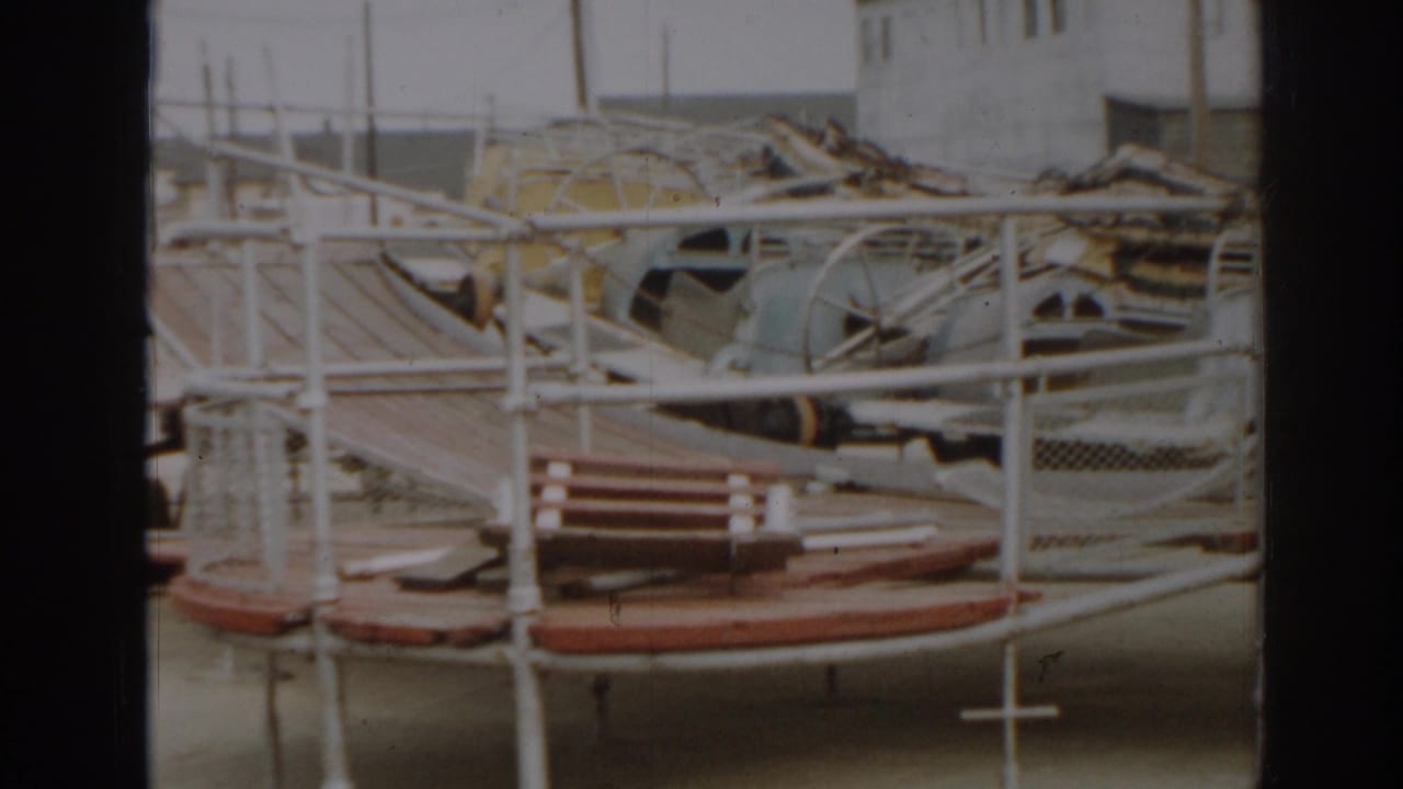 Wrecked boat frames and railings piled near a waterfront building.