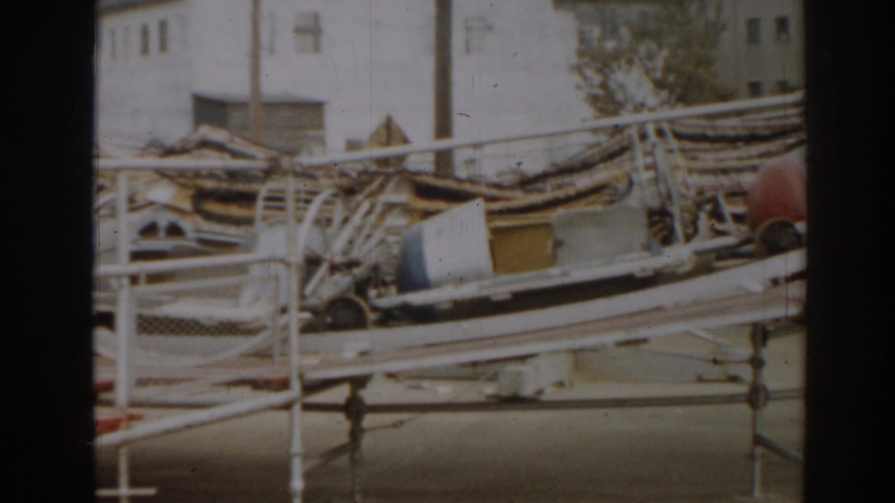 Boat wreckage, railings, and debris with a building in the background.