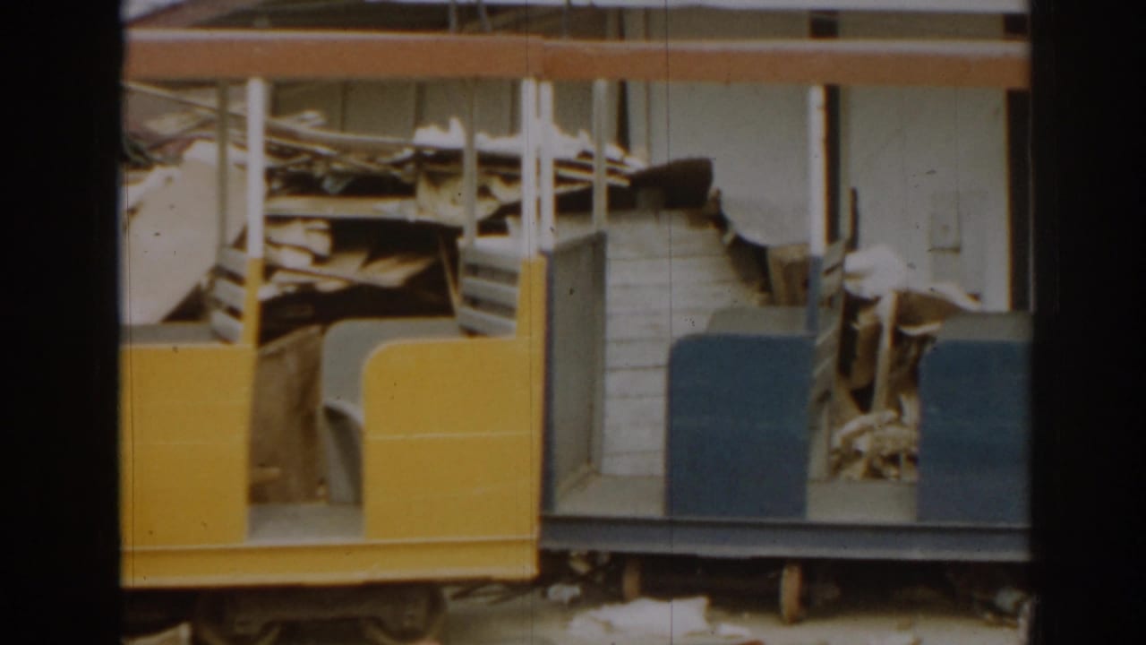 Damaged yellow and blue miniature train car with exposed seats and interior structure.
